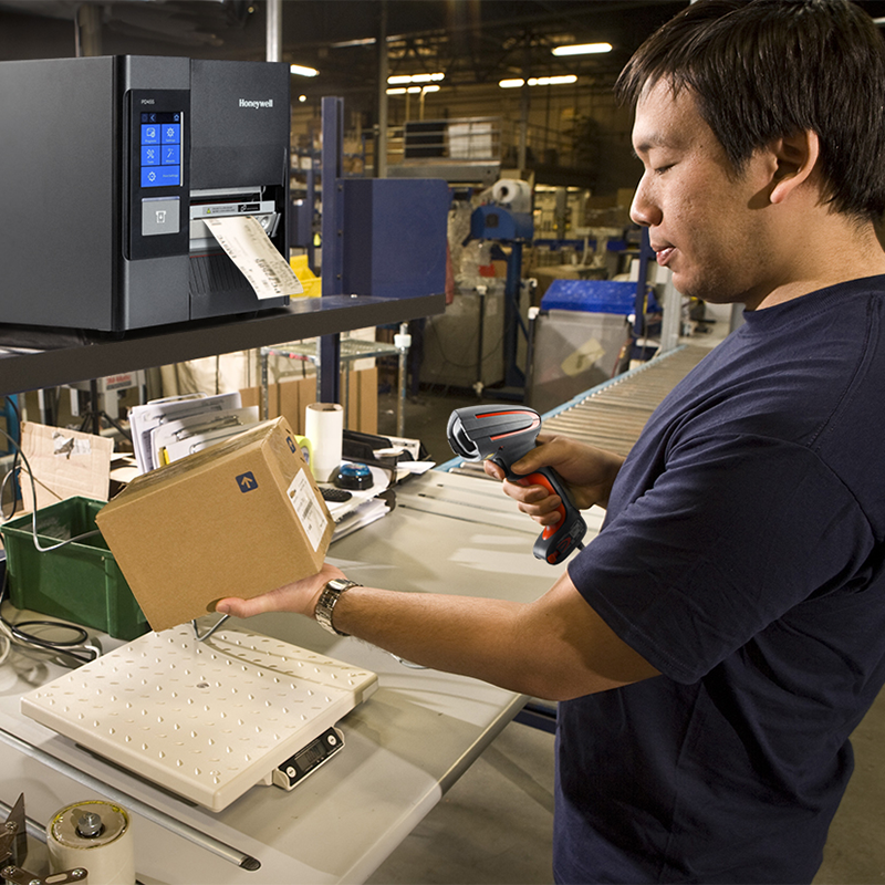 Person using a barcode scanner in a warehouse setting with industrial equipment.