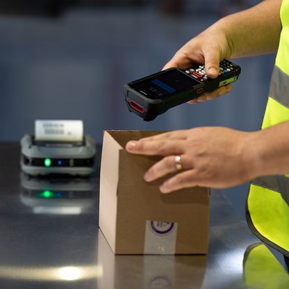 Person scanning a cardboard box with a handheld device in a warehouse setting.
