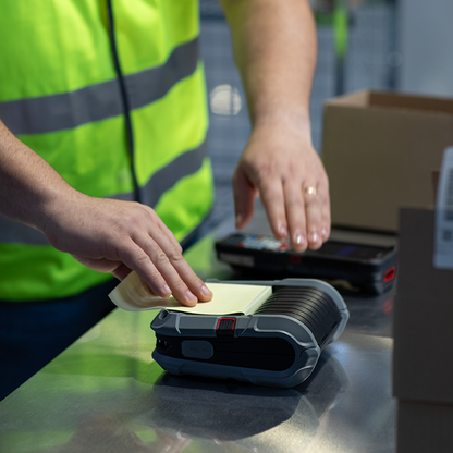 Person in a high-visibility vest using a thermal printer with a box in the background