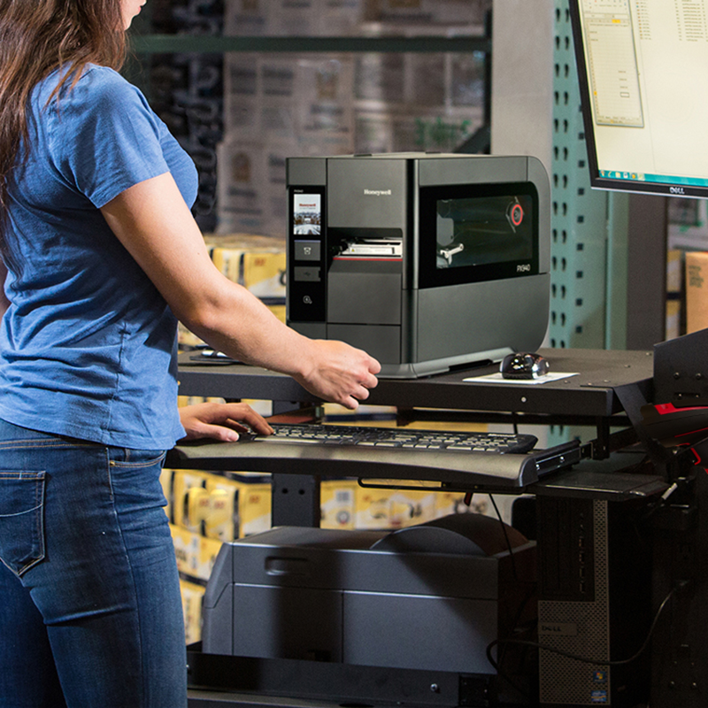 Person using a computer in a warehouse setting with a printer and monitor. PX940